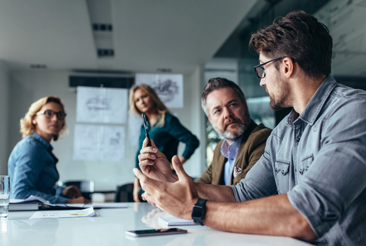 A diverse team of professionals in an open-plan office meeting, collectively discussing strategic benefits and positive outcomes derived from workplace psychometric testing and skill alignment.