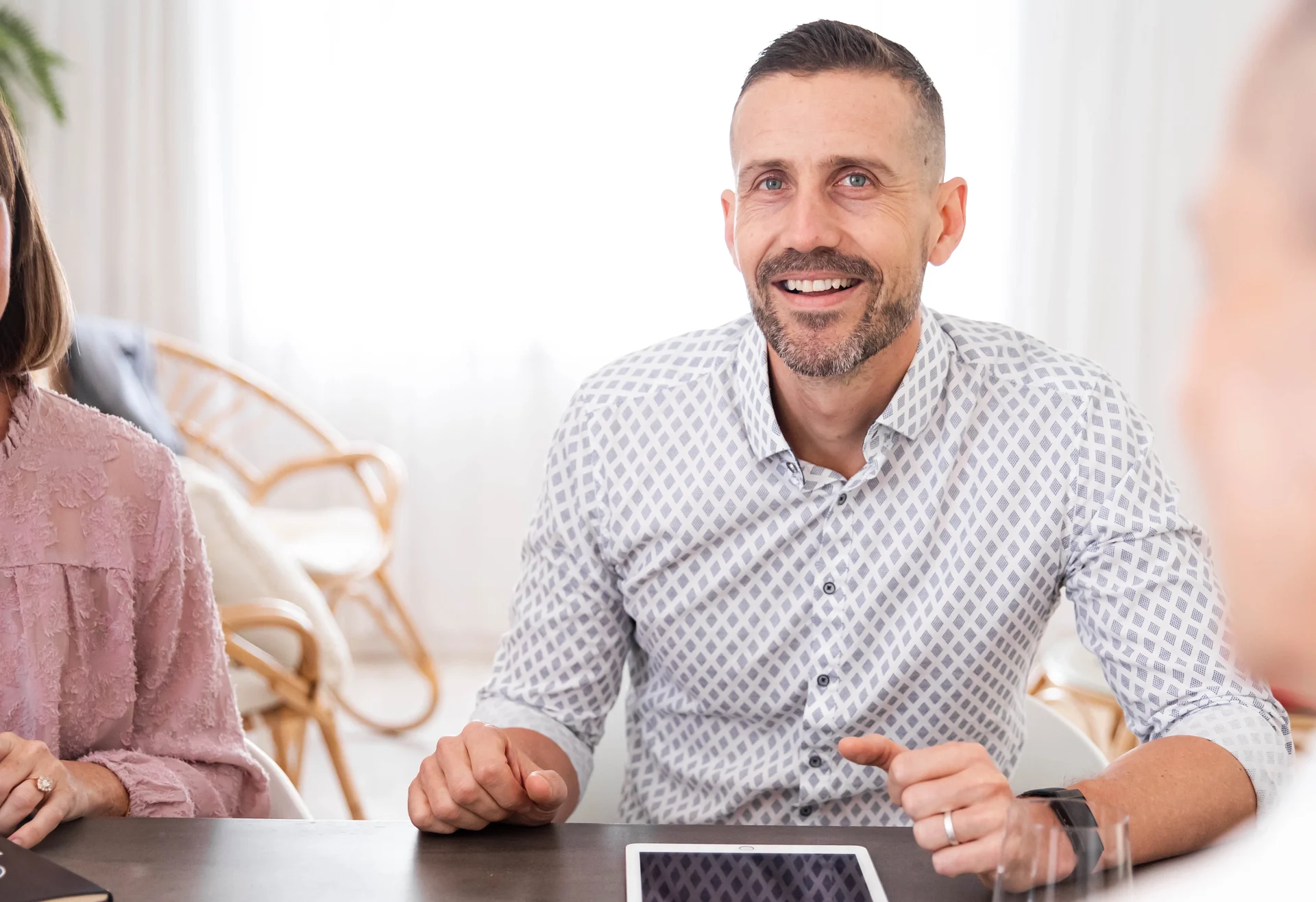A smiling male professional engaging in a leadership support session. He is seated at a table with a tablet and notebook, appearing attentive and positive during a collaborative meeting for the Future Fit Leaders Program.